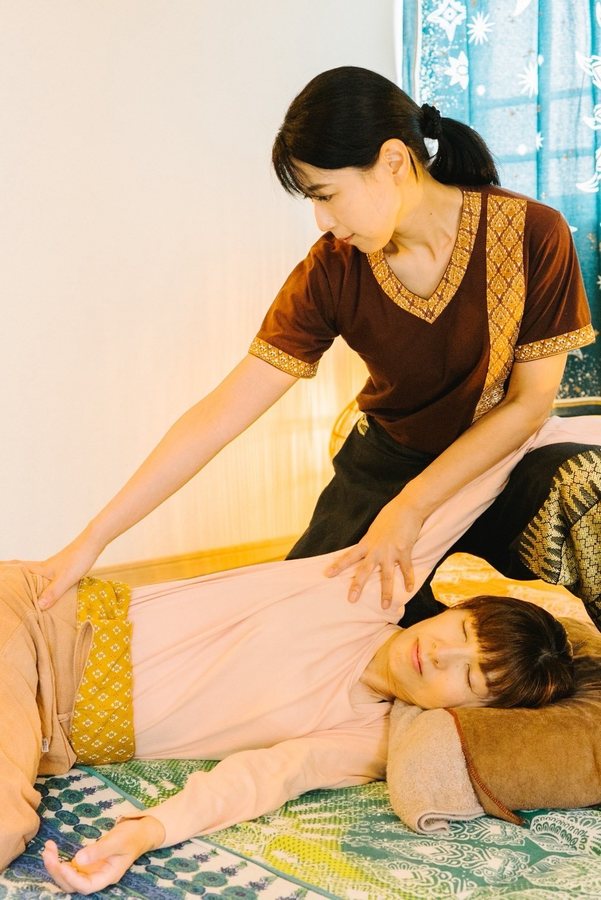 タイの施術着を着たセラピストが、脚のストレッチ施術を行っている